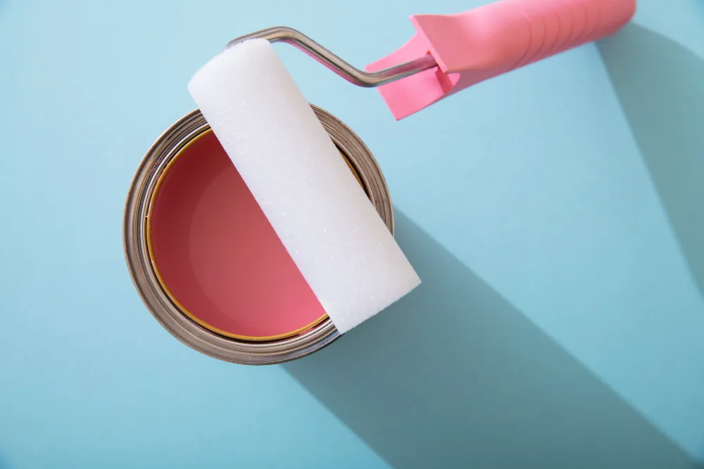 Rolo de pintura em lata cheio de tinta rosa sobre fundo azul.